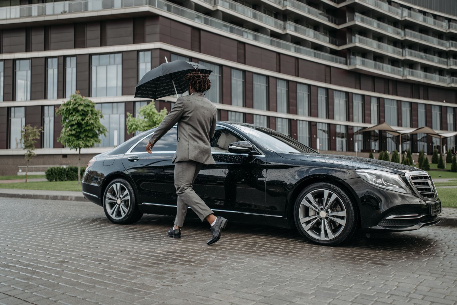 Man in a grey suit opening the door of a black car